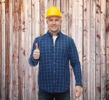 repair, construction, building, people and maintenance concept - smiling male builder or manual worker in helmet showing thumbs up over wooden fence background