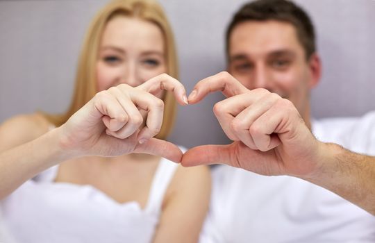 love, people and happiness concept - close up of smiling couple in bed making heart shape gesture