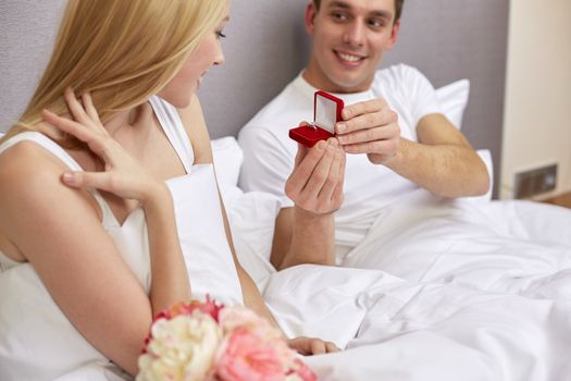 proposal, people, love, holidays and happiness concept - close up of happy man giving woman little red gift box with engagement ring