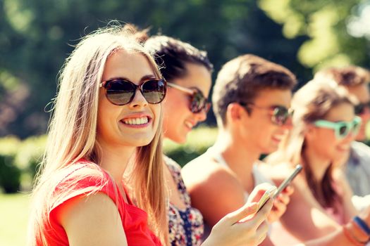 friendship, leisure, summer, technology and people concept - group of smiling friends with smartphones sitting in park