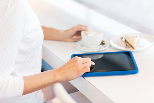 leisure, people, technology and lifestyle concept - close up of young woman hands with tablet pc computer drinking coffee and eating cake at cafe