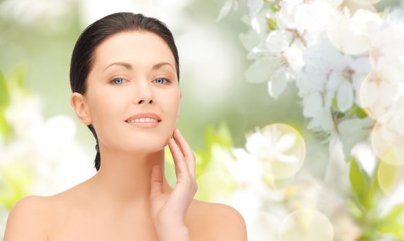 beauty, people and health concept - beautiful young woman touching her face over green blooming garden background