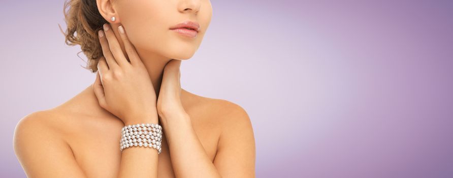 beauty, people and jewelry concept - close up of beautiful woman with pearl earrings and bracelet over violet background