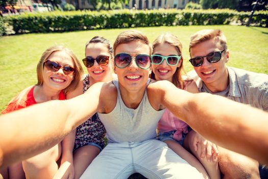 friendship, leisure, summer, technology and people concept - group of smiling friends making selfie with smartphone camera or tablet pc in park