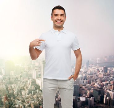 happiness, advertisement, fashion, gesture and people concept - smiling man in t-shirt pointing finger on himself over city background