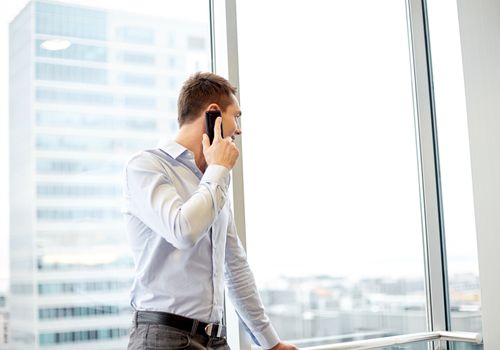 business, technology and people concept - happy businessman calling on smartphone and looking out office window