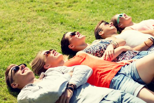 friendship, leisure, summer and people concept - group of smiling friends lying on grass outdoors