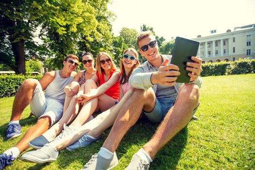 friendship, leisure, summer, technology and people concept - group of smiling friends with tablet pc computer sitting and making selfie in park