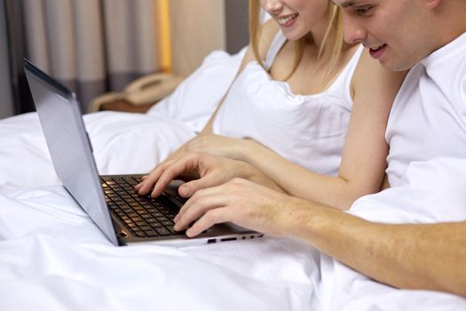 people, bedtime, technology and relations concept - close up of smiling couple in bed with laptop computer typing and networking