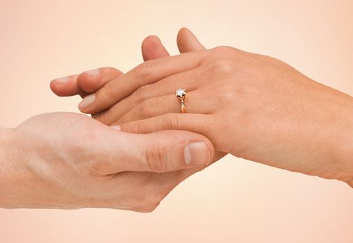 jewelry, couple, love and wedding concept - close up of man and woman hands with engagement ring over beige background