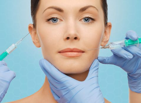 plastic surgery, injections and beauty concept - beautiful young woman face and surgeon hands with syringes over blue background