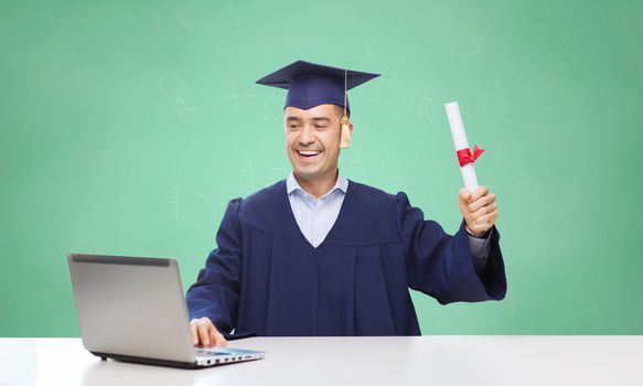 education, graduation, technology and people concept - happy adult student in mortarboard with diploma and laptop computer sitting at table over green school chalk board background