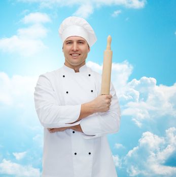 cooking, profession and people concept - happy male chef cook holding rolling pin over blue sky with clouds background