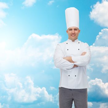 cooking, profession and people concept - happy male chef cook with crossed hands over blue sky with clouds background