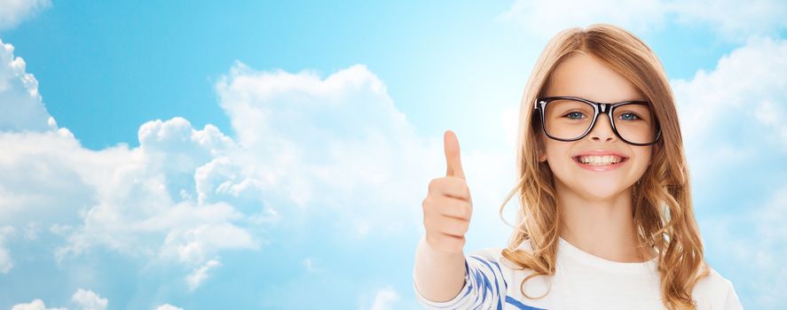 education, school, childhood, people and vision concept - smiling cute little girl with black eyeglasses showing thumbs up gesture over blue sky and white clouds background