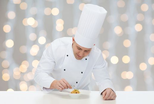 cooking, profession, haute cuisine, food and people concept - happy male chef cook decorating dish over christmas holidays lights background