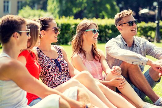 friendship, leisure, summer and people concept - group of smiling friends outdoors sitting on grass in park