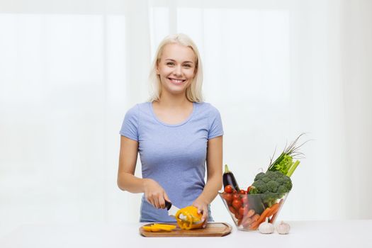 healthy eating, vegetarian food, cooking, dieting and people concept - smiling young woman chopping vegetables at home