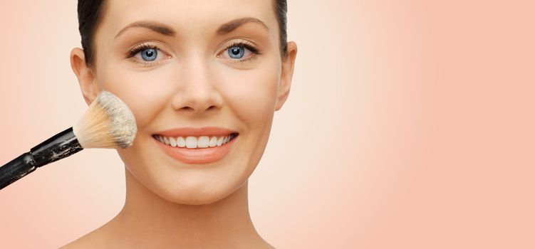 beauty, people and makeup concept - happy woman face applying powder foundation with brush over beige background