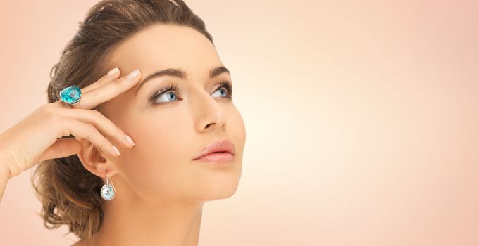 beauty, jewelry, people and accessories concept - close up of woman face with cocktail ring on hand and earrings over beige background