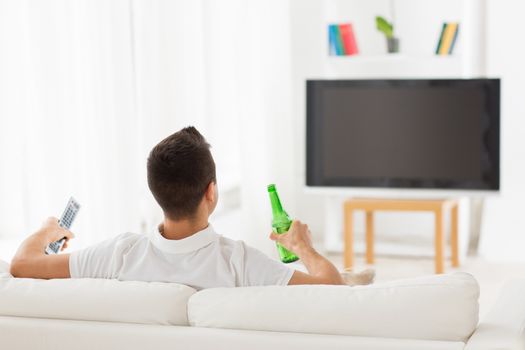 leisure, technology, mass media and people concept - man watching tv and drinking bottle beer at home from back