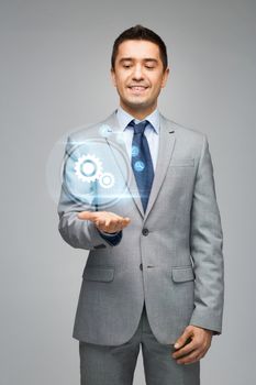 business, people and technology concept - happy businessman in suit showing or holding virtual projection of computer settings on hand palm over gray background