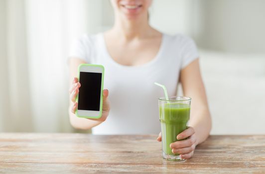 healthy eating, diet, detox, technology and people concept - close up of woman with smartphone green juice sitting at wooden table