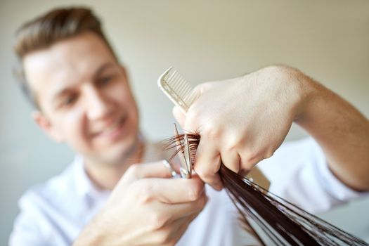 beauty, hairstyle and people concept - male stylist hands with scissors and comb cutting hair tips at salon