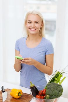 healthy eating, vegetarian food, dieting and people concept - smiling young woman with smartphone cooking vegetables at home
