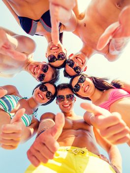 friendship, summer vacation, holidays, gesture and people concept - group of smiling friends wearing swimwear standing in circle and showing thumbs up over blue sky