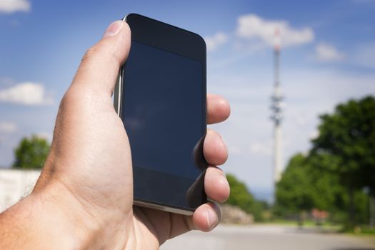 Image of hand with mobile phone and broadcasting tower in the background