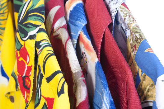 Closeup selection of five colorful yellow, red, blue and green Hawaiian shirts arranged on hangers on white background