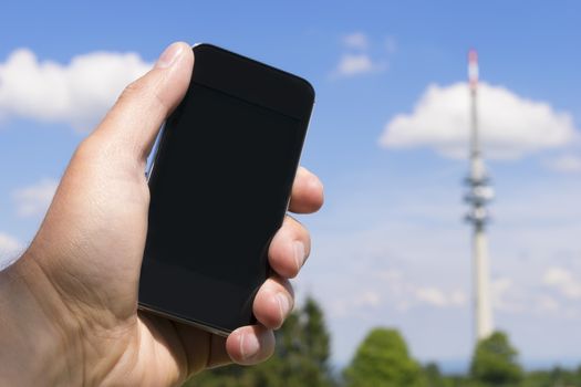 Image of hand with mobile phone and broadcasting tower in the background