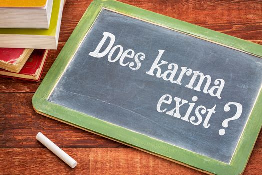 Does karma exist? A question in a white chalk  on a vintage blackboard with a stack of books against rustic wooden table