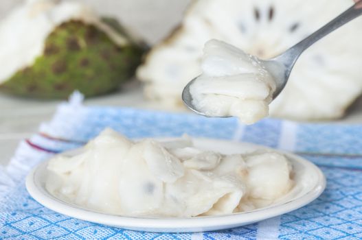 Serving of delicious raw soursop fruit on plate and spoonful with whole cut fruit in background