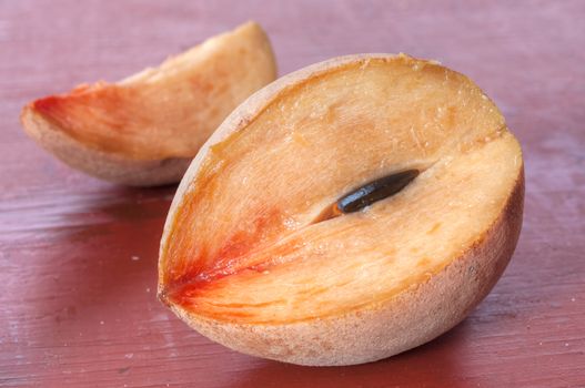 Closeup of ripe cut sapodilla chicozapote fruit and slice on red table