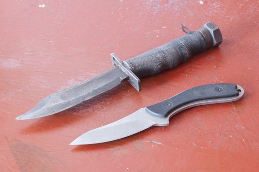 Old used bowie knife and fixed blade field knife on red rustic table top