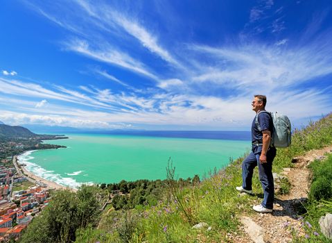 Smiling man with backpack looking at Cefalu city, Italy