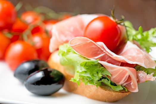 thin slices of prosciutto with mixed olives and tomato on bread