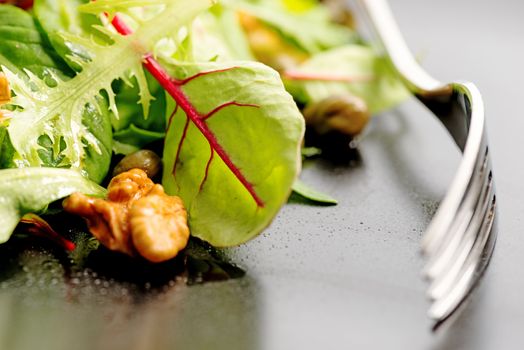 Fresh ecological salad mix with nuts on black plate, macro