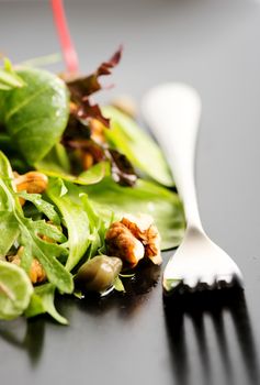 Fresh ecological salad mix with nuts on black plate, macro