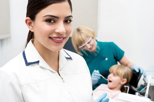 Smiling dentist, assistant examining a patient behind