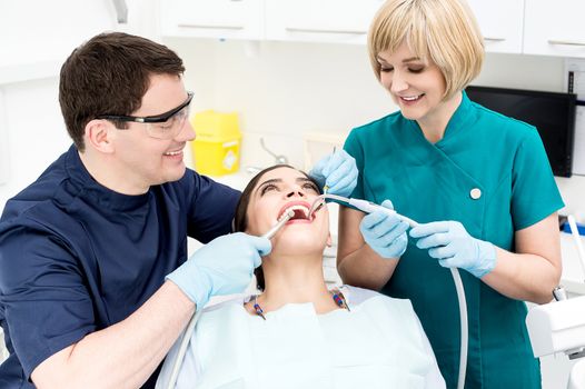 Male dentist treating patient teeth with assistant