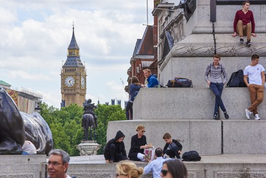 LONDON, UK - JUNE 15: Tourists sitting on the steps of Trafalgar Square, with Big Ben in the background. June 15, 2015 in London.