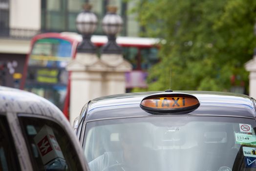 LONDON, UK - JUNE 15: Cropped shot with taxi sign lit on traditional black cab, with red routemaster in the background. June 15, 2015 in London.