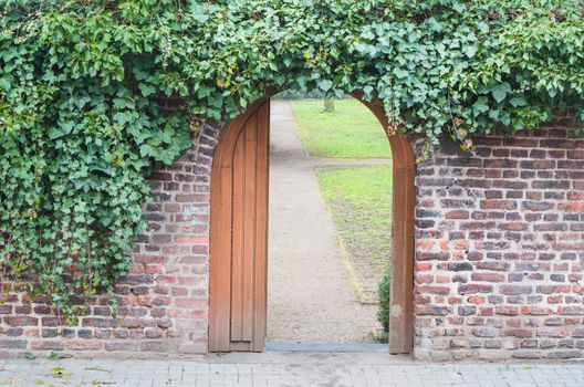 An entrance gate in a wall into a park. Behind the open door is a way.
