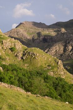 A view across a spur to a rocky mountainside with, in the distance, the ridgeline of Crib Goch, Snowdonia, Wales, UK.