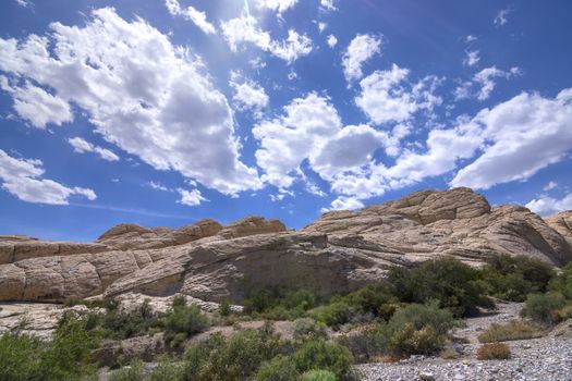 Aztec sandstone geological rock formations along seasonal wash under blue sky with cumulus clouds during sping in Red Rock national conservation area, Nevada