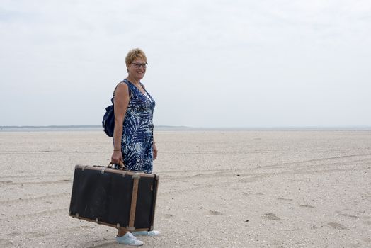 woman with old vintage used suitcase walking on the beach