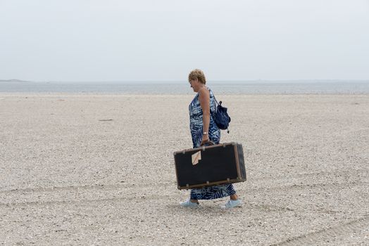 woman with old vintage used suitcase walking near the beach